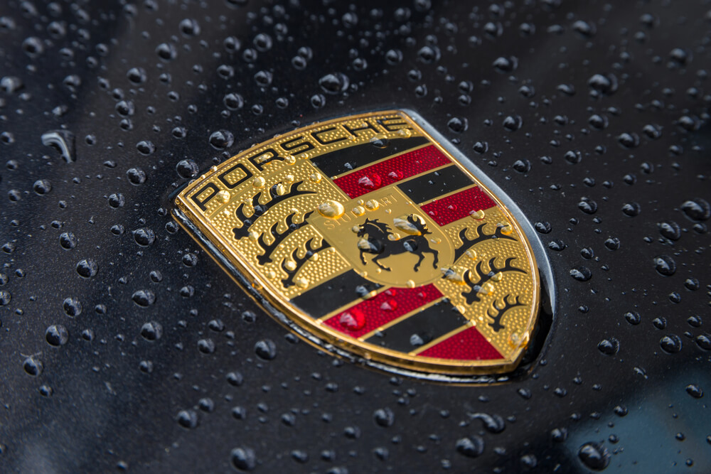 Close-up of a Porsche logo on a wet car hood, covered in raindrops.