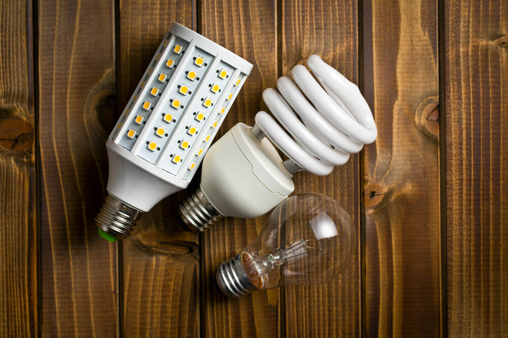 Energy-efficient LED, CFL, and incandescent light bulbs on wooden background.