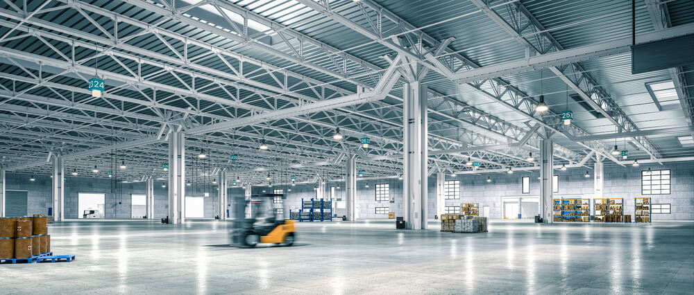 Spacious industrial warehouse interior with high ceilings, forklift in motion, and organized shelves of goods.