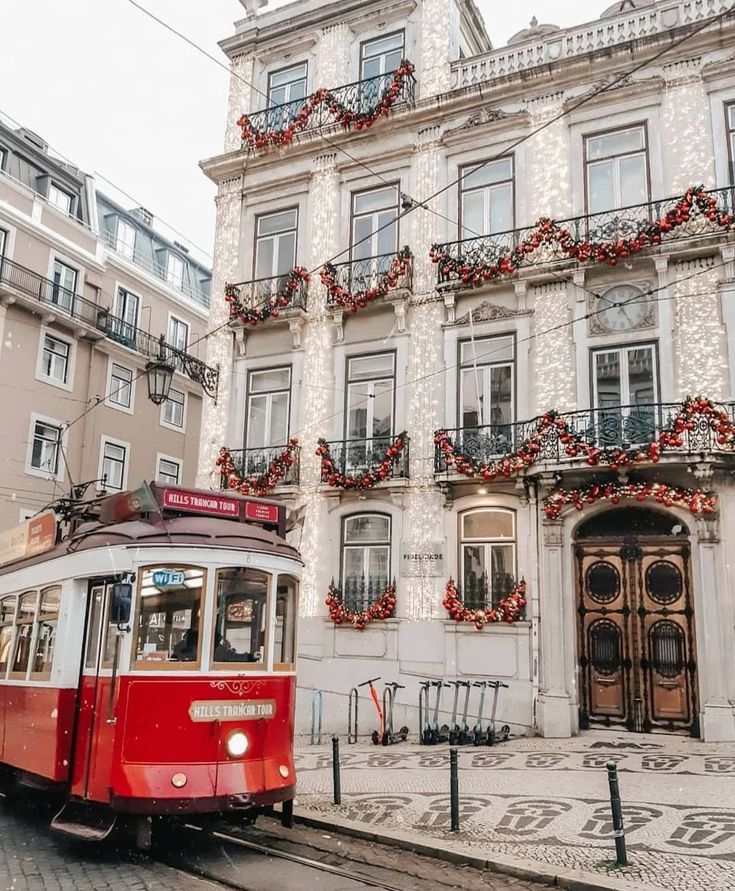 Red tram passing a beautifully decorated historic building with Christmas garlands in an urban setting.