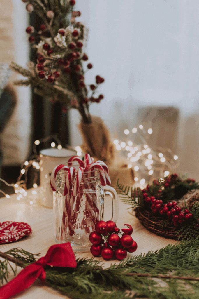 Festive Christmas decor with candy canes, fir branches, red berries, and lights on a cozy table setting.