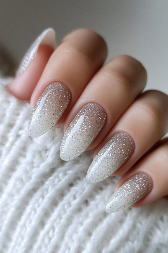 Glittery ombre manicure on almond-shaped nails, perfect for a chic and elegant winter look against a cozy sweater.