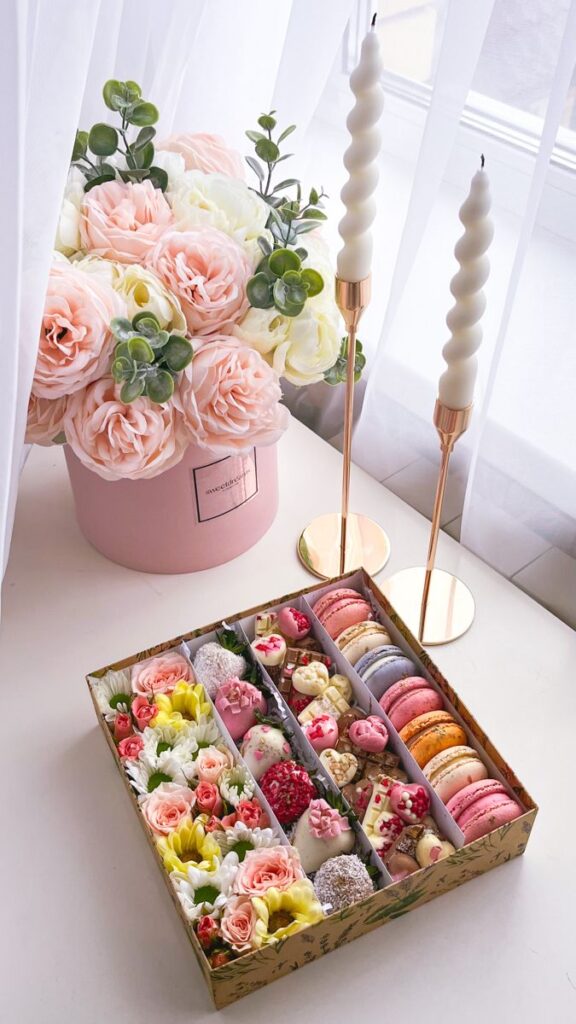 Elegant floral arrangement and assorted macarons with sweets on a table, accompanied by spiral candles for a chic decor.