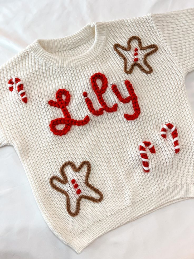 White knit sweater with Lily in red letters, adorned with candy canes and gingerbread men decorations. Perfect for holidays.