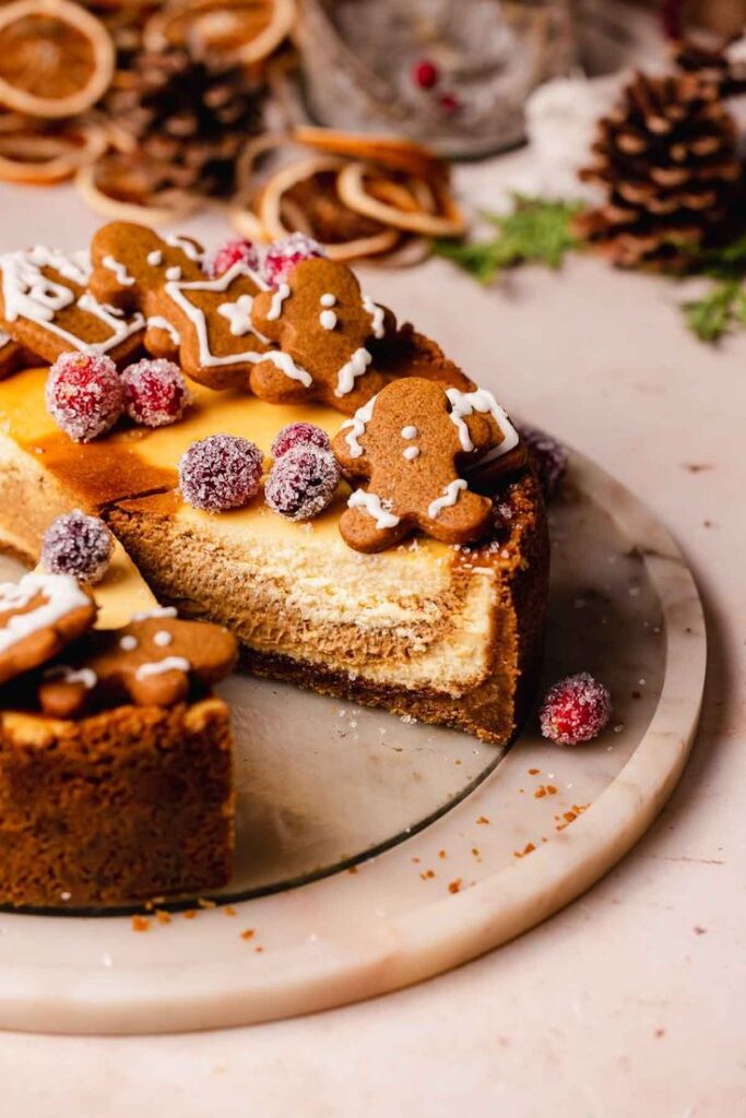 Festive cheesecake topped with gingerbread cookies and sugared cranberries on a marble platter.