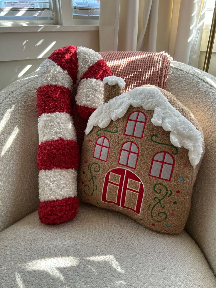 Cozy holiday decor: Gingerbread house and candy cane pillows on a beige chair by a sunny window.