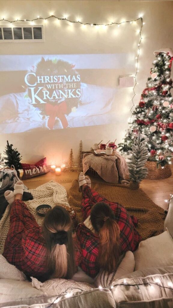 Cozy home theater setup with Christmas tree and lights, watching Christmas with the Kranks in pajamas.