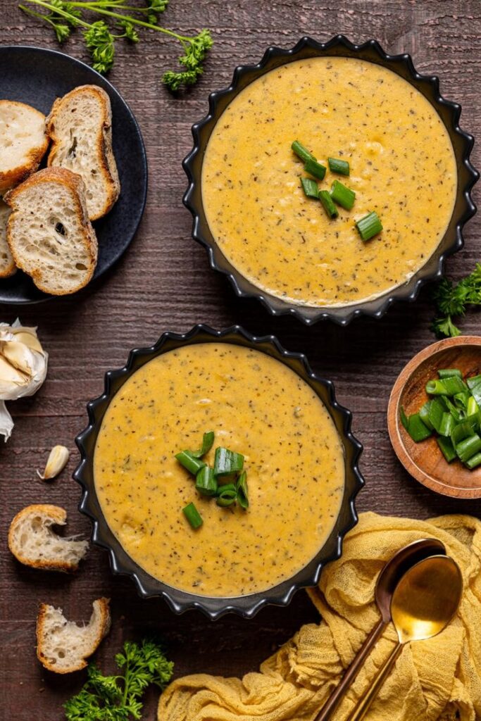 Creamy soup garnished with green onions in black bowls, served with sliced bread.