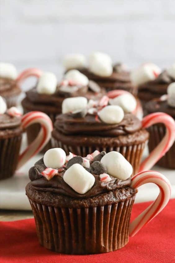 Chocolate cupcakes with marshmallows and candy cane handles on a red napkin, perfect for the holidays.