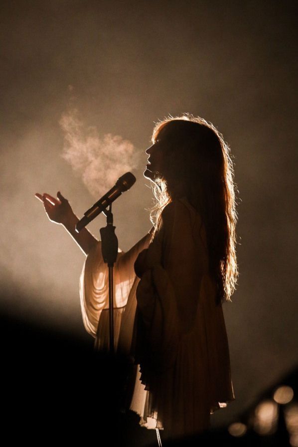 Singer performing on stage with dramatic lighting and visible breath in a dark, atmospheric setting.