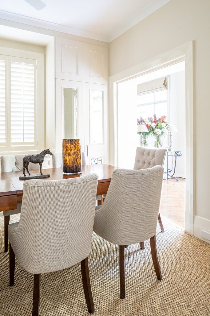 Elegant dining room with modern chairs, wood table, horse sculpture, and floral arrangement in bright natural light.