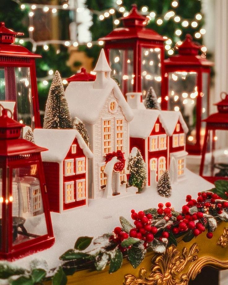 Festive holiday village display with snow-covered houses, red lanterns, and berry decorations, glowing under warm lights.