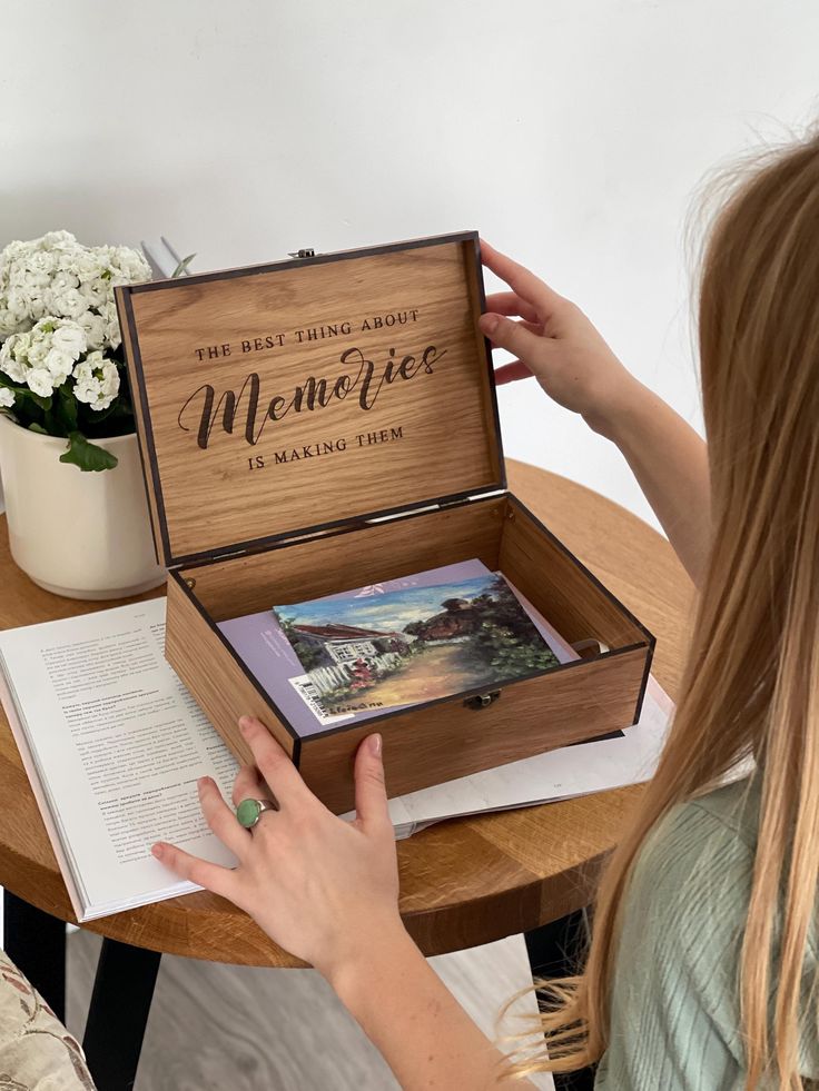 Woman opening a wooden box with The best thing about memories is making them on the lid, holding postcards.