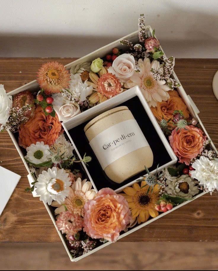 Elegant floral box with Carpe Diem candle centerpiece on wooden table.