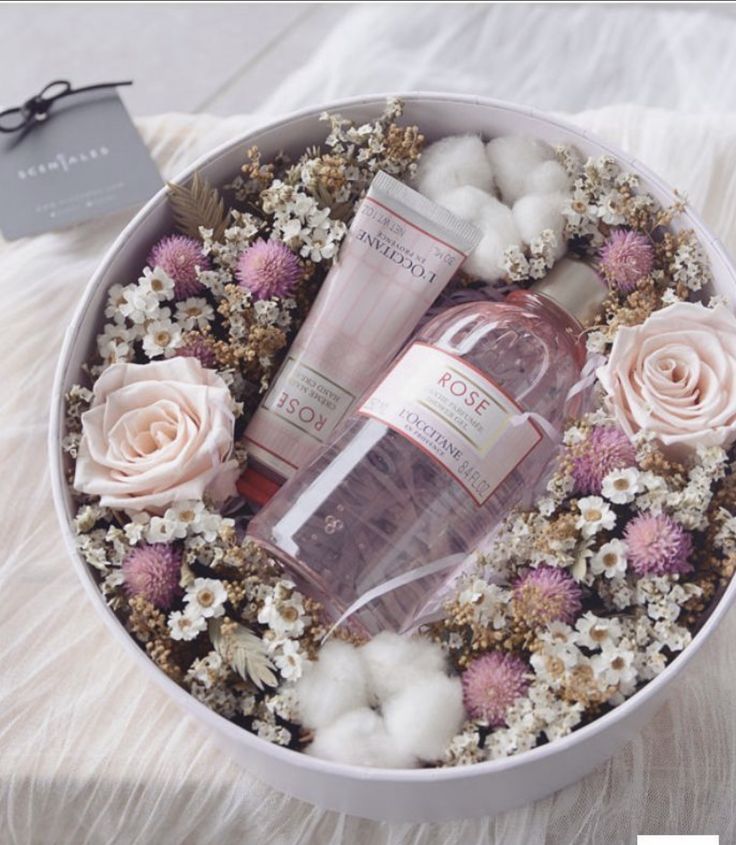 Gift box with rose-scented L'Occitane products surrounded by pastel flowers and delicate white blooms.