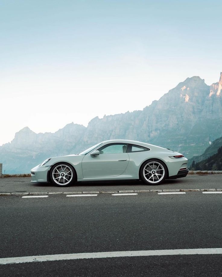 Sleek white sports car on mountain road with scenic backdrop and clear sky.