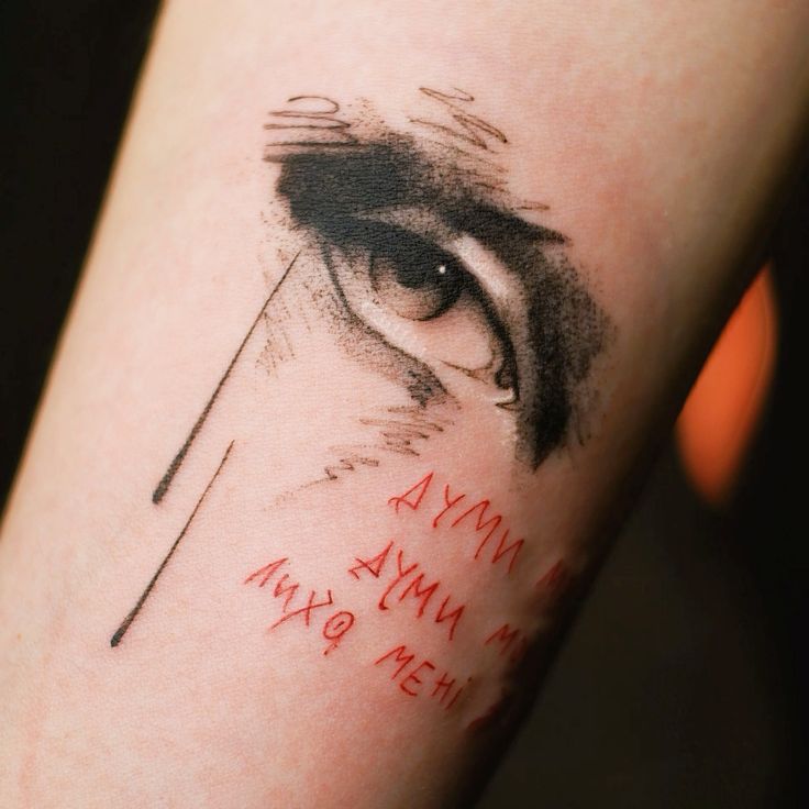 Artistic eye tattoo with red text detail on forearm, showcasing unique design and intricate linework.