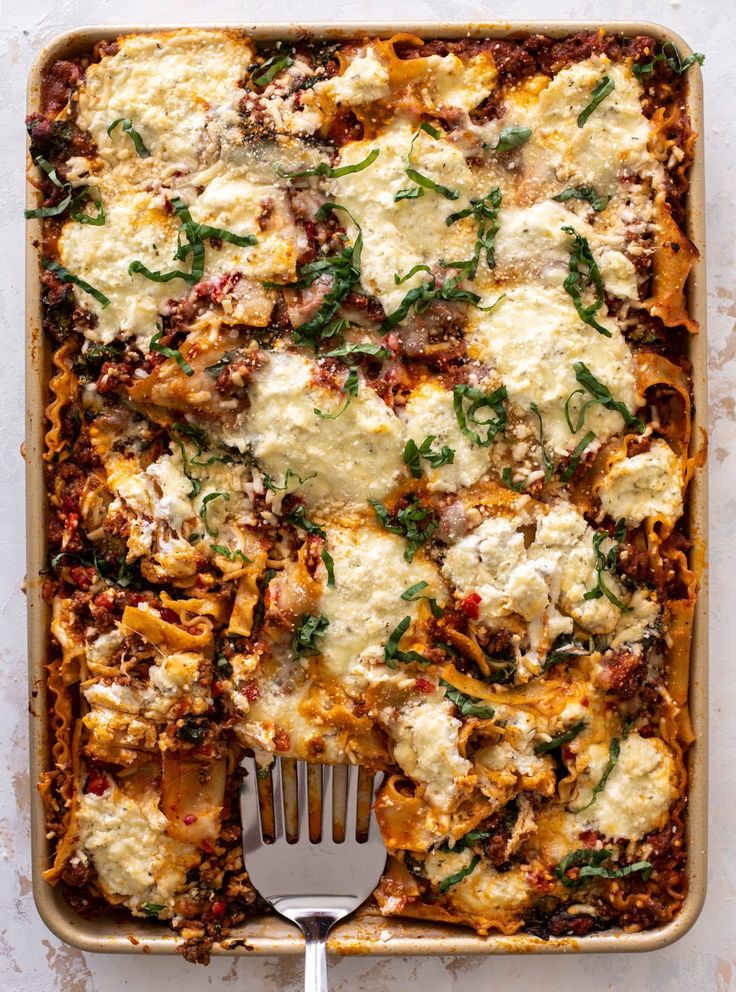 Cheesy baked lasagna with fresh herbs and a spatula, viewed from above in a baking dish.