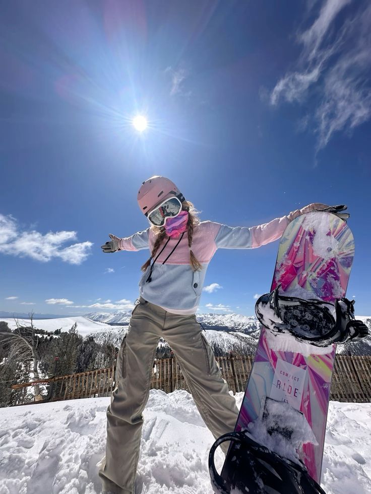 Snowboarder in colorful gear enjoys a sunny day on the snowy mountain slopes, posing triumphantly with her snowboard.