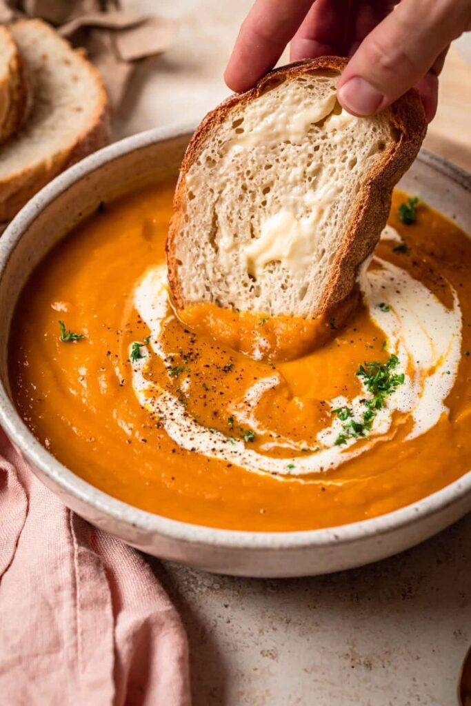 Creamy pumpkin soup with a swirl of cream and fresh bread for dipping. Perfect for cozy autumn meals.