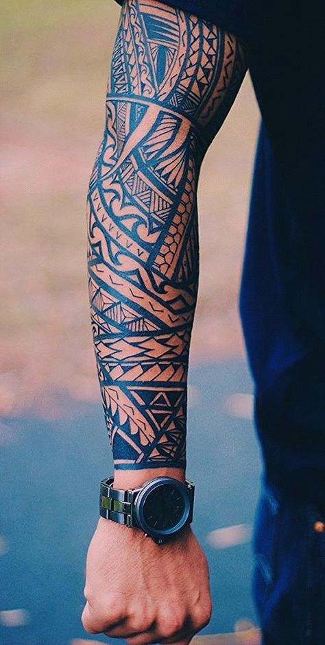 Arm with intricate tribal sleeve tattoo and stylish watch, outdoors in natural light.