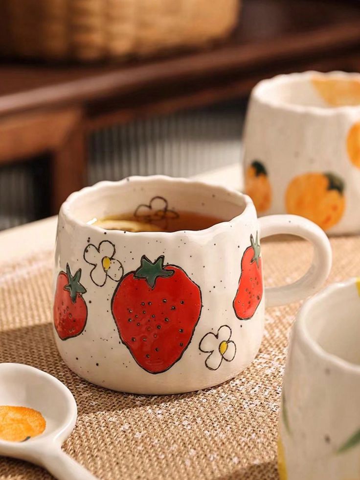 Handcrafted ceramic mug with strawberry design filled with tea, on a woven mat.