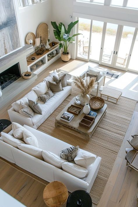 Modern coastal living room with white sofas, natural decor, and large windows overlooking a beach setting.