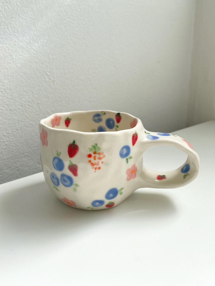 Colorful fruit and flower patterned ceramic mug on white table.