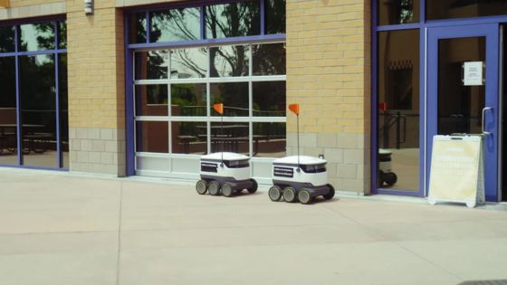 Two delivery robots outside a building with glass doors, reflecting urban automation and modern technology.