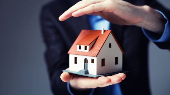 Hands protecting a small house model, symbolizing home insurance or security.