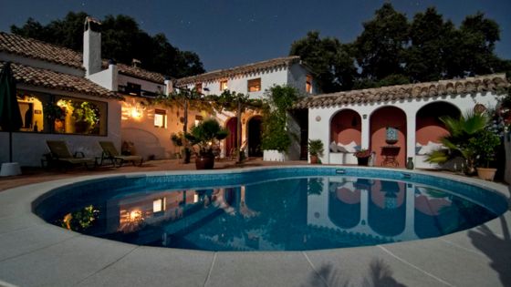 Charming villa with a pool under a starlit sky, surrounded by lush greenery and warm ambient lighting.