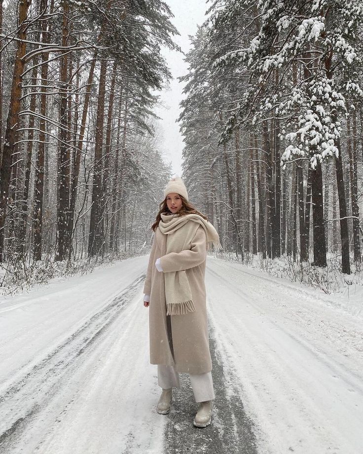 Woman in a winter coat walking through a snow-covered forest path, surrounded by tall, snow-laden trees.