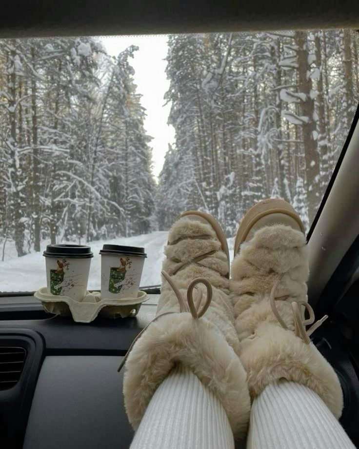 Cozy boots on car dashboard, snowy forest drive with hot drinks. Winter road trip vibes.