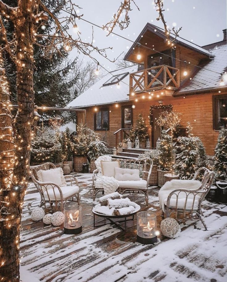 Cozy winter patio with string lights, snow-covered furniture, and a wooden house in the background.