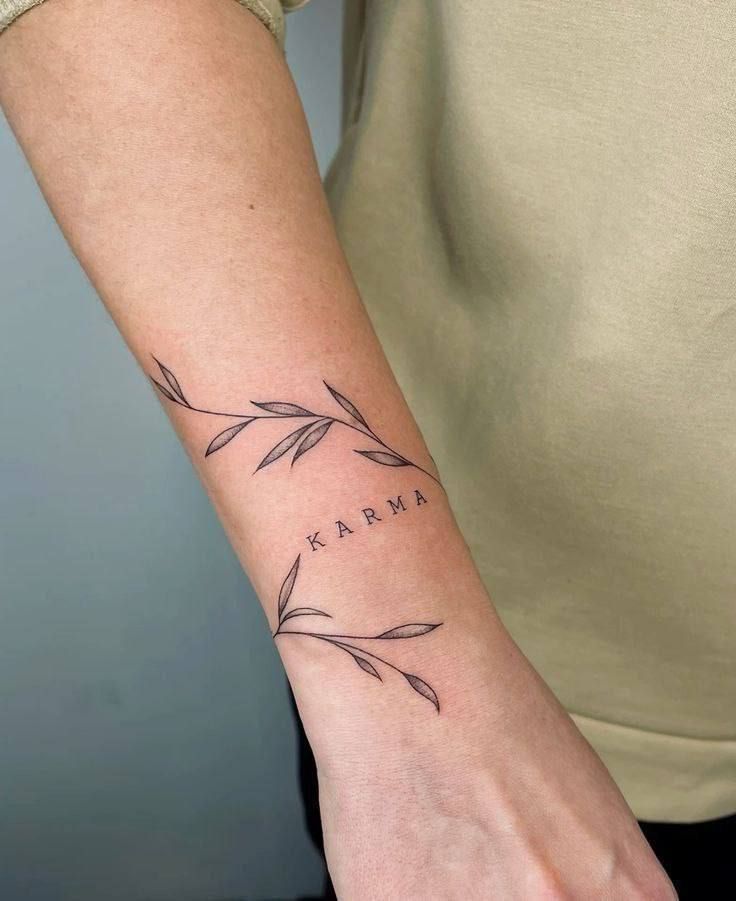 Minimalist tattoo with the word Karma and delicate leaf design on a forearm.