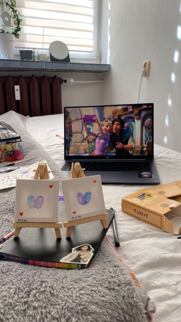 Canvas art on mini easels in cozy room with laptop showing animated movie, tarot box nearby.