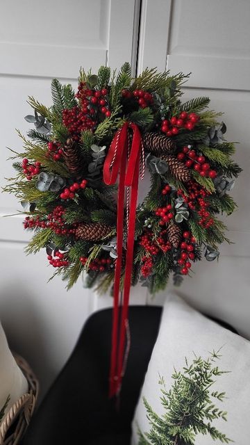 Festive holiday wreath with pine cones, red berries, and a red ribbon, hanging on a white door.