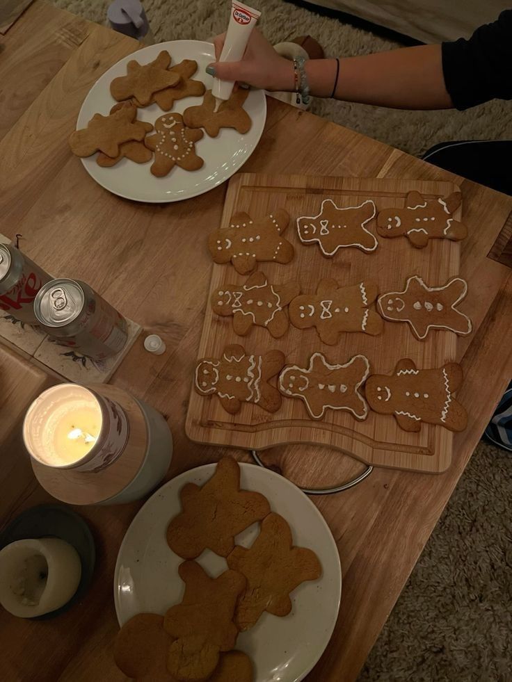 Decorating gingerbread cookies on a wooden table with a lit candle and refreshing drinks nearby. Perfect holiday setup.