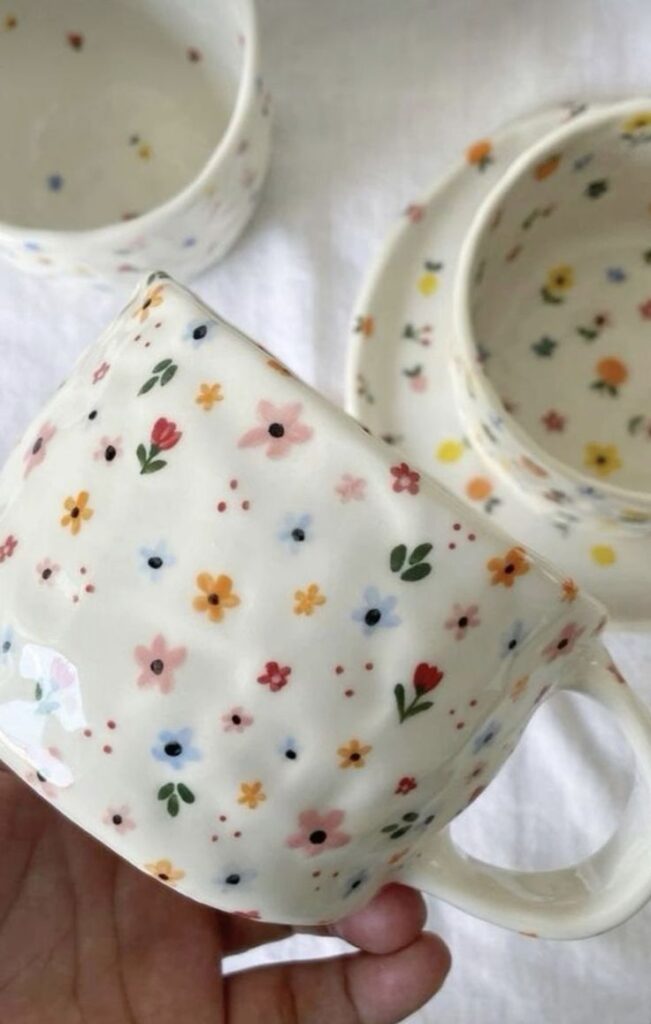 Hand-painted floral ceramic cup set on a white background, showcasing delicate multicolored flower patterns.