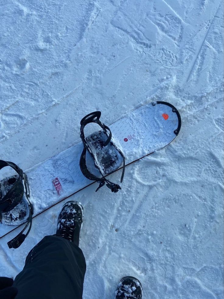 Snowboard resting on snowy ground with boots nearby, ready for an exciting ride on the slopes.