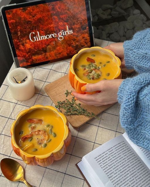 Cozy autumn scene with pumpkin soup, a lit candle, and a tablet streaming a show on a checkered tablecloth.