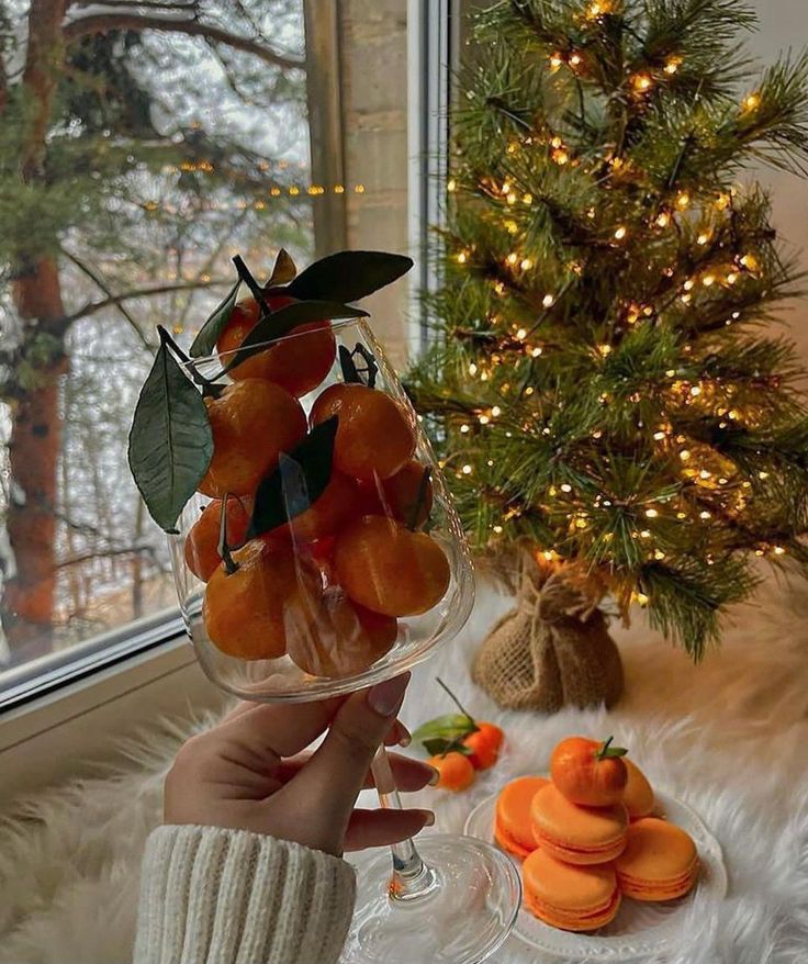 Cozy winter scene with mandarins in a glass and an illuminated Christmas tree by the window.