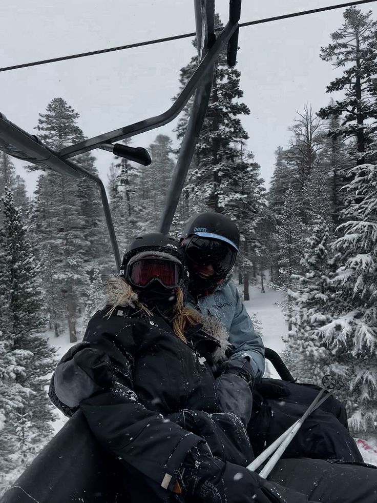 Two skiers on a snowy chairlift surrounded by snow-covered trees, enjoying a winter day outdoors.