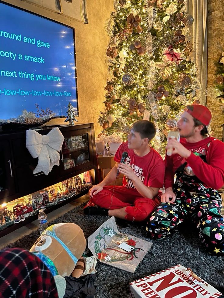 Two people singing karaoke by a Christmas tree, enjoying a festive holiday atmosphere with decorations.