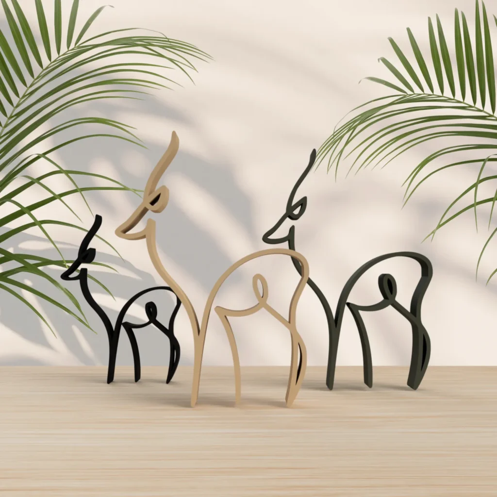 Minimalist deer sculptures on a wooden table with green palm leaves in the background.