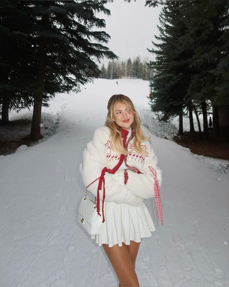 Woman in cozy winter attire standing on a snowy path with pine trees in the background.