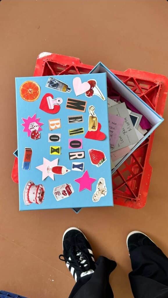 Colorful memory box decorated with vibrant stickers, placed on red crate, filled with handwritten notes.