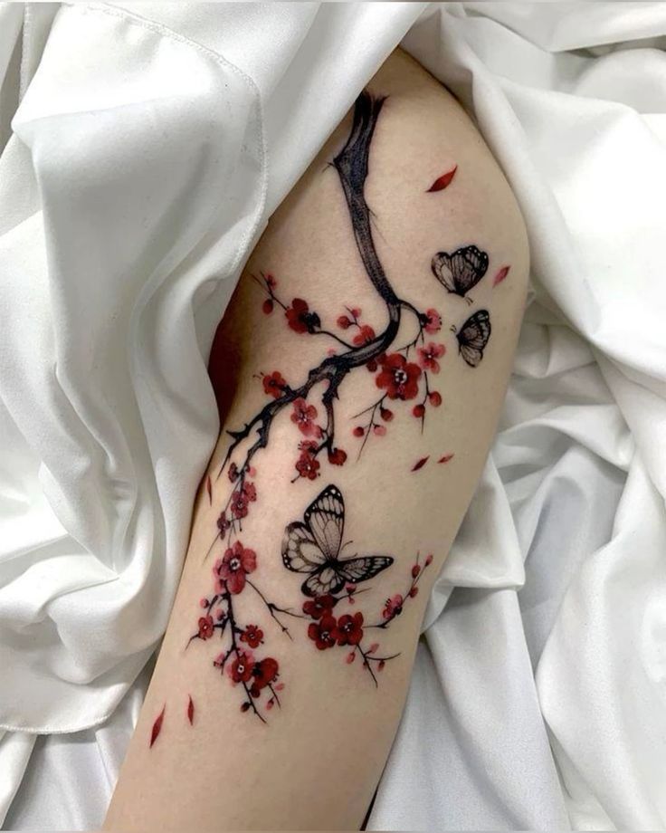 Cherry blossom branch tattoo with butterflies on an arm, draped in white fabric.