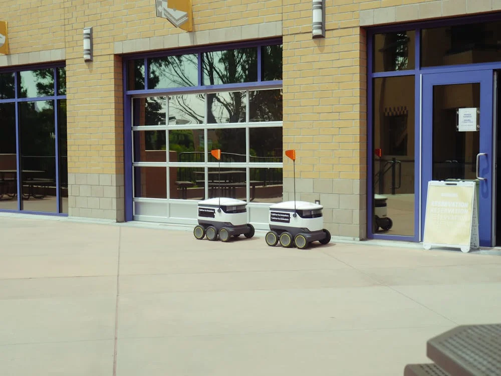 Two delivery robots outside a modern building, showcasing automated technology in urban environments.