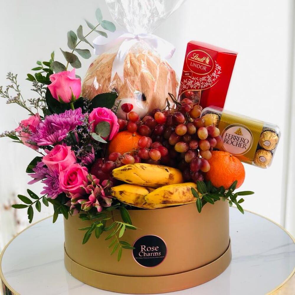 Gift basket with roses, bananas, grapes, chocolates, and bread, beautifully arranged in a decorative round box.